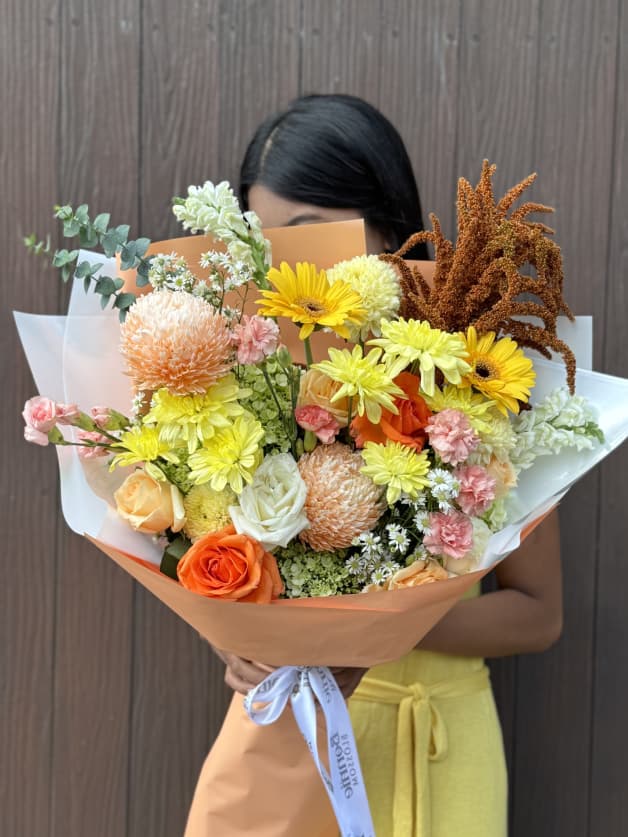 A warm, textured bouquet featuring orange roses, yellow gerberas, and peach chrysanthemums